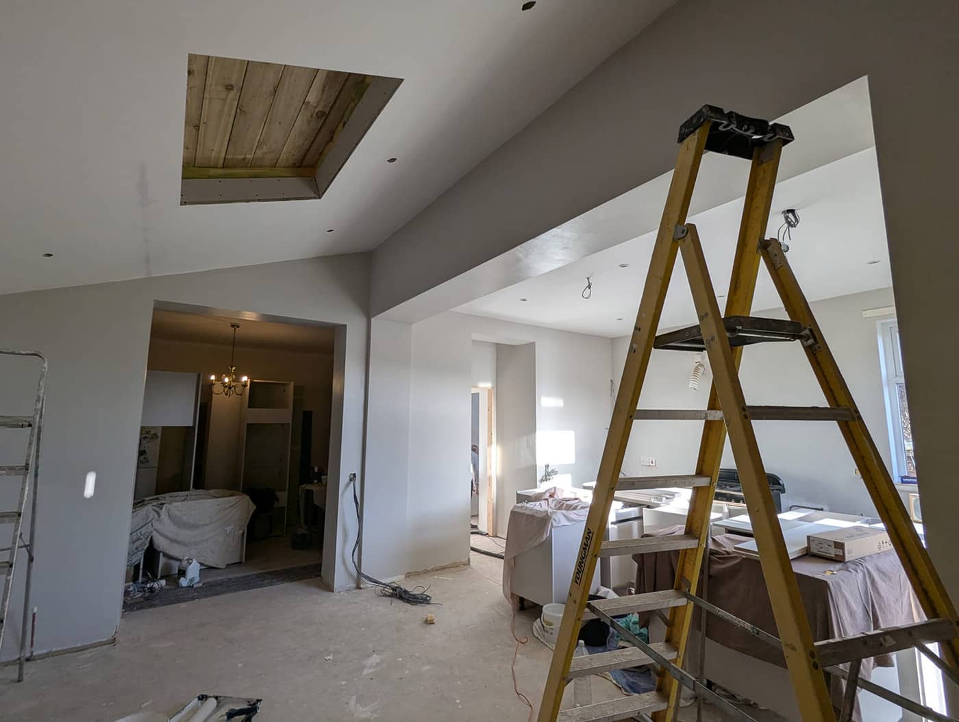 Inside the extension during fit-out: a wide new opening through to the original house, a boxed-in beam and a roof light opening in the vaulted ceiling